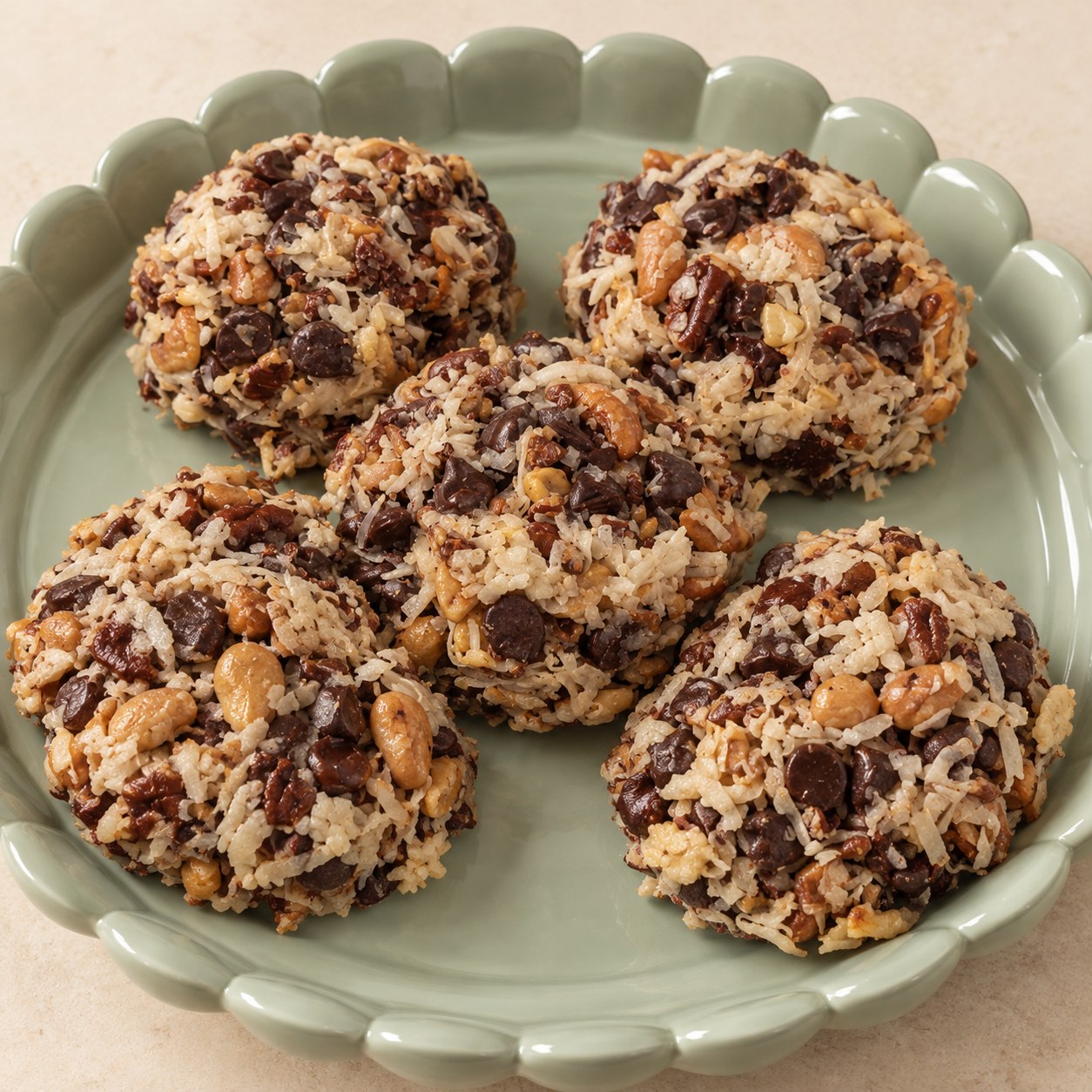 Five Magic Cookies with shredded coconut, chocolate chips, cashews, and pecans on a pale green scalloped platter.