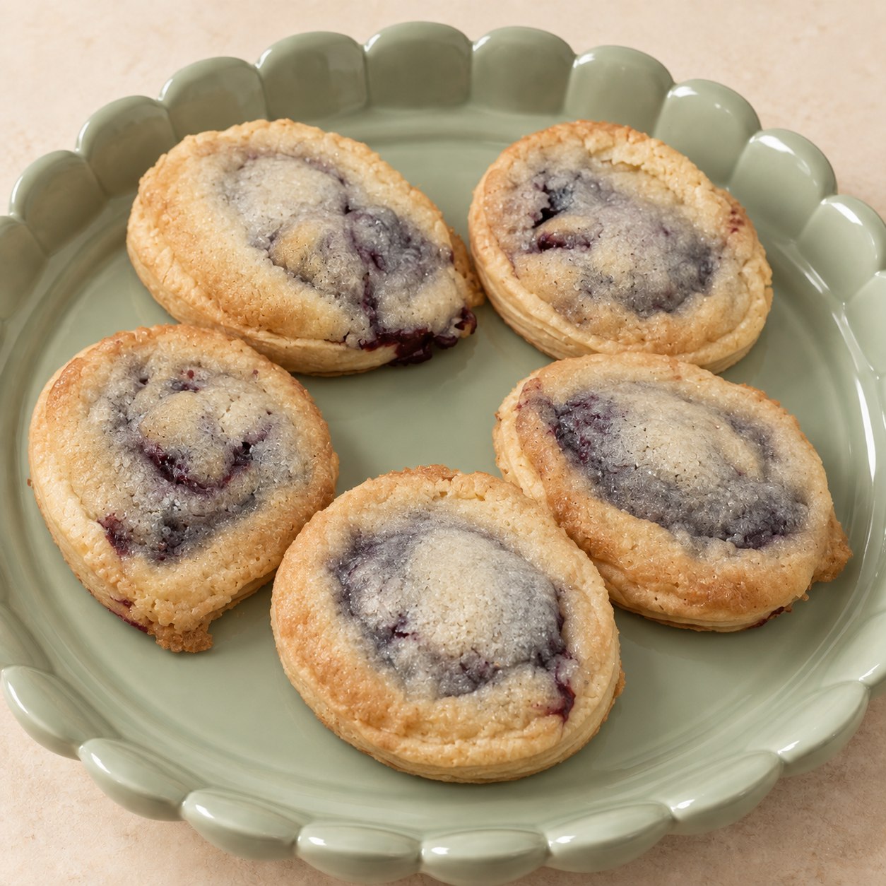 Golden pie cookies with purple fruit filling beneath a tender cookie topping, arranged on a pale green scalloped platter.